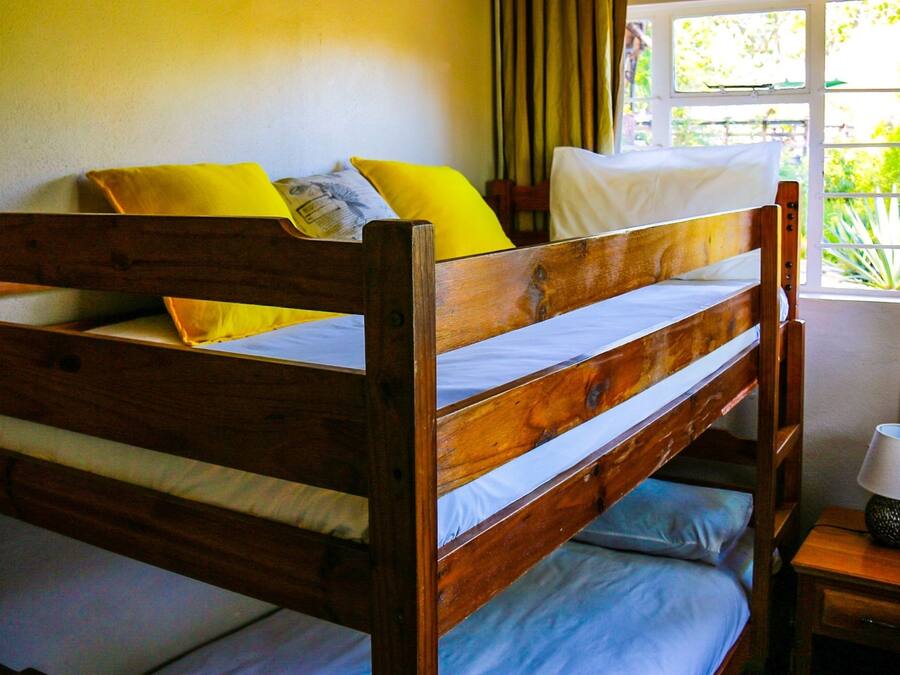 A wooden bunk bed with two pillows, a bedside lamp, and a window with curtains.