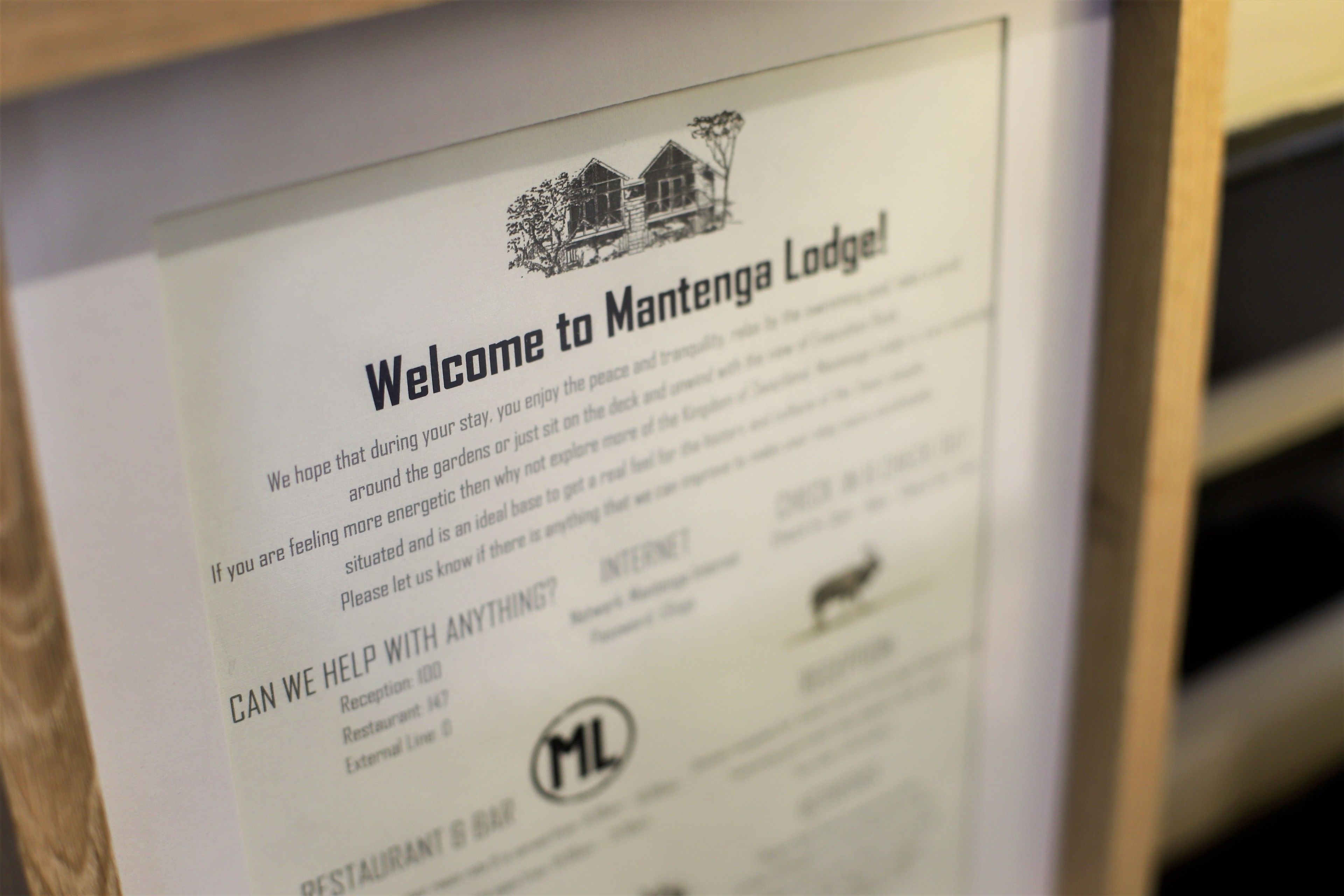 Un letrero de bienvenida para Mantenga Lodge con una ilustración de una casa, número de recepción y un logotipo.