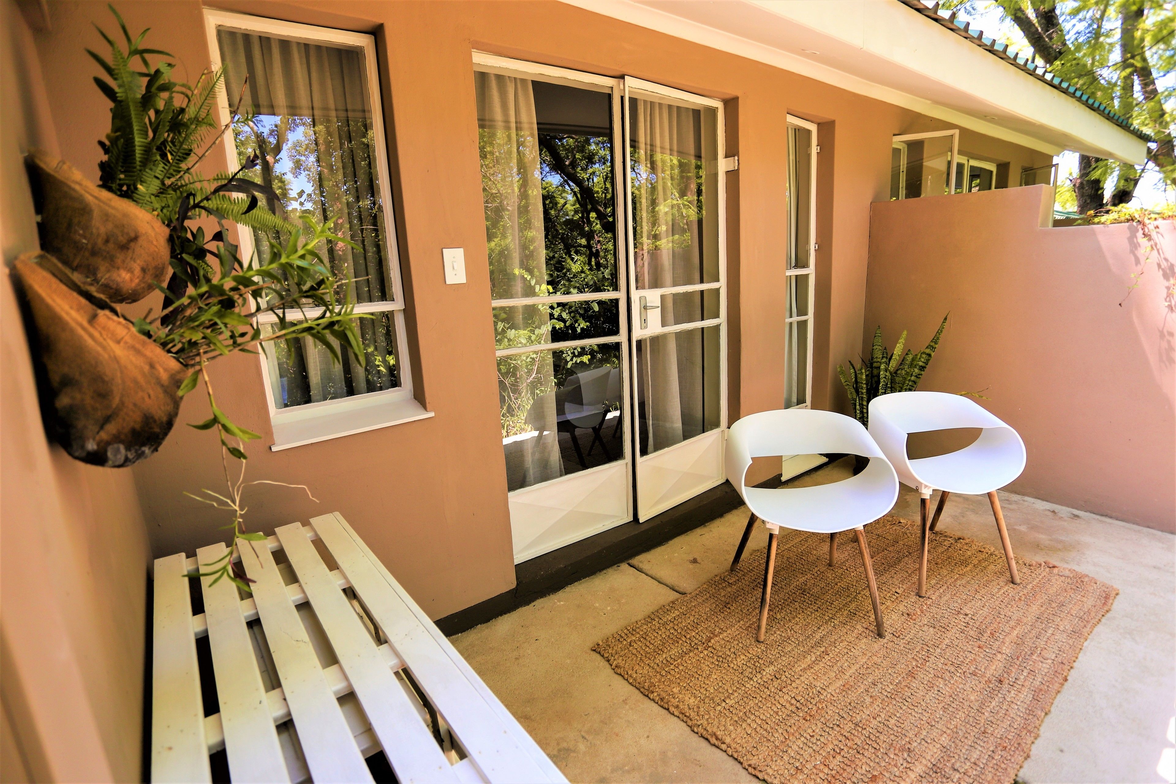 A balcony with a white bench, two white chairs, and a woven rug.