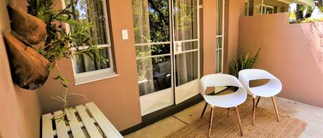 A balcony with a white bench, two white chairs, and a woven rug.