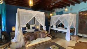A room with two four-poster beds with white canopies, a wooden sofa, a coffee table with books, and a cowhide rug. - Jafferji House (Zanzibar Town)