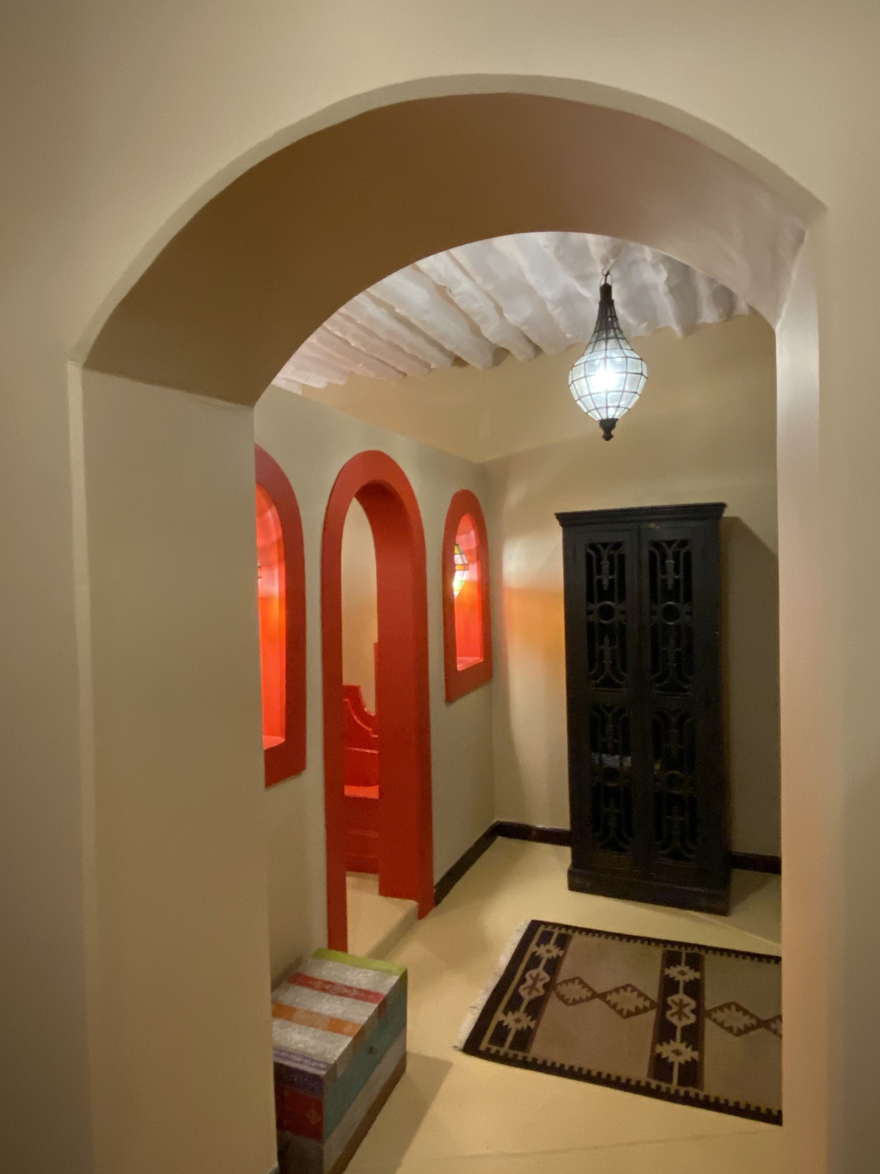 Un pasillo con techo blanco, arcos rojos, un armario de madera y un tapete estampado.