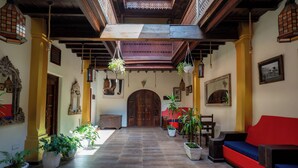 A spacious hallway with a wooden ceiling, potted plants, a red sofa, and a wooden door at the end. - Jafferji House (Zanzibar Town)