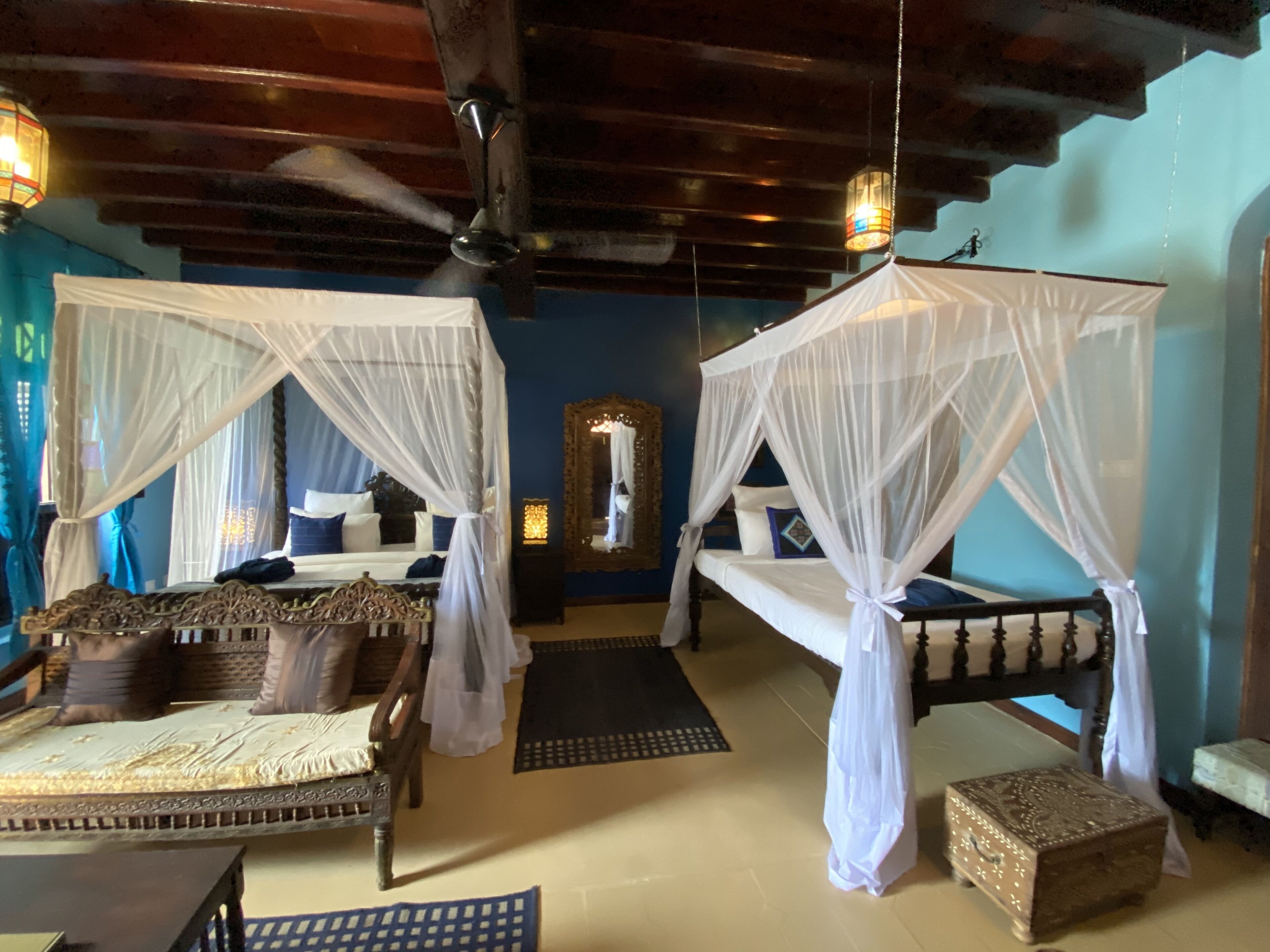 A room with two beds, each with a canopy, a wooden headboard, and a nightstand. There is a mirror on the wall and a small table with a chair.