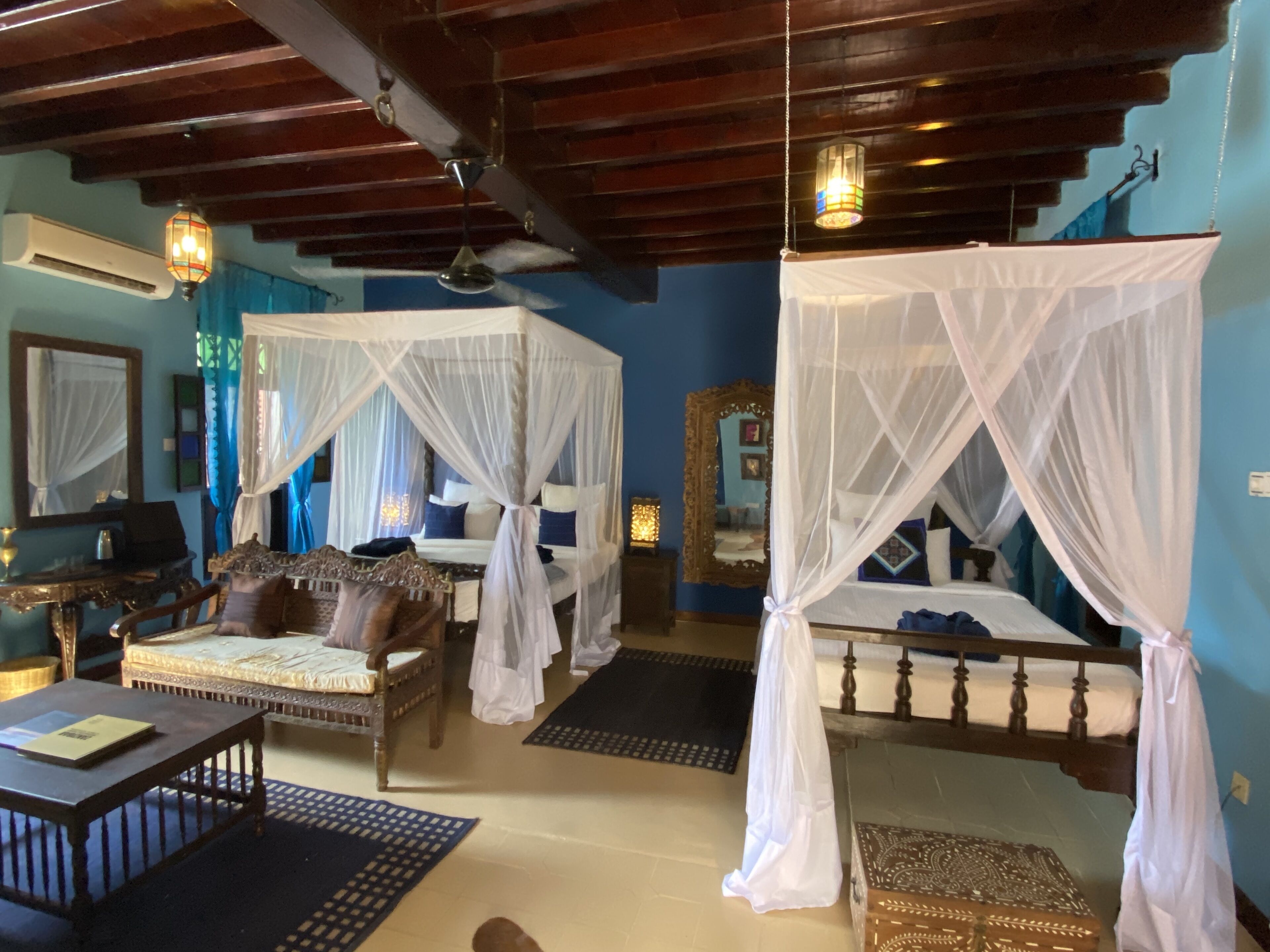 A room with two beds, each with a canopy, a wooden table, and a chair.