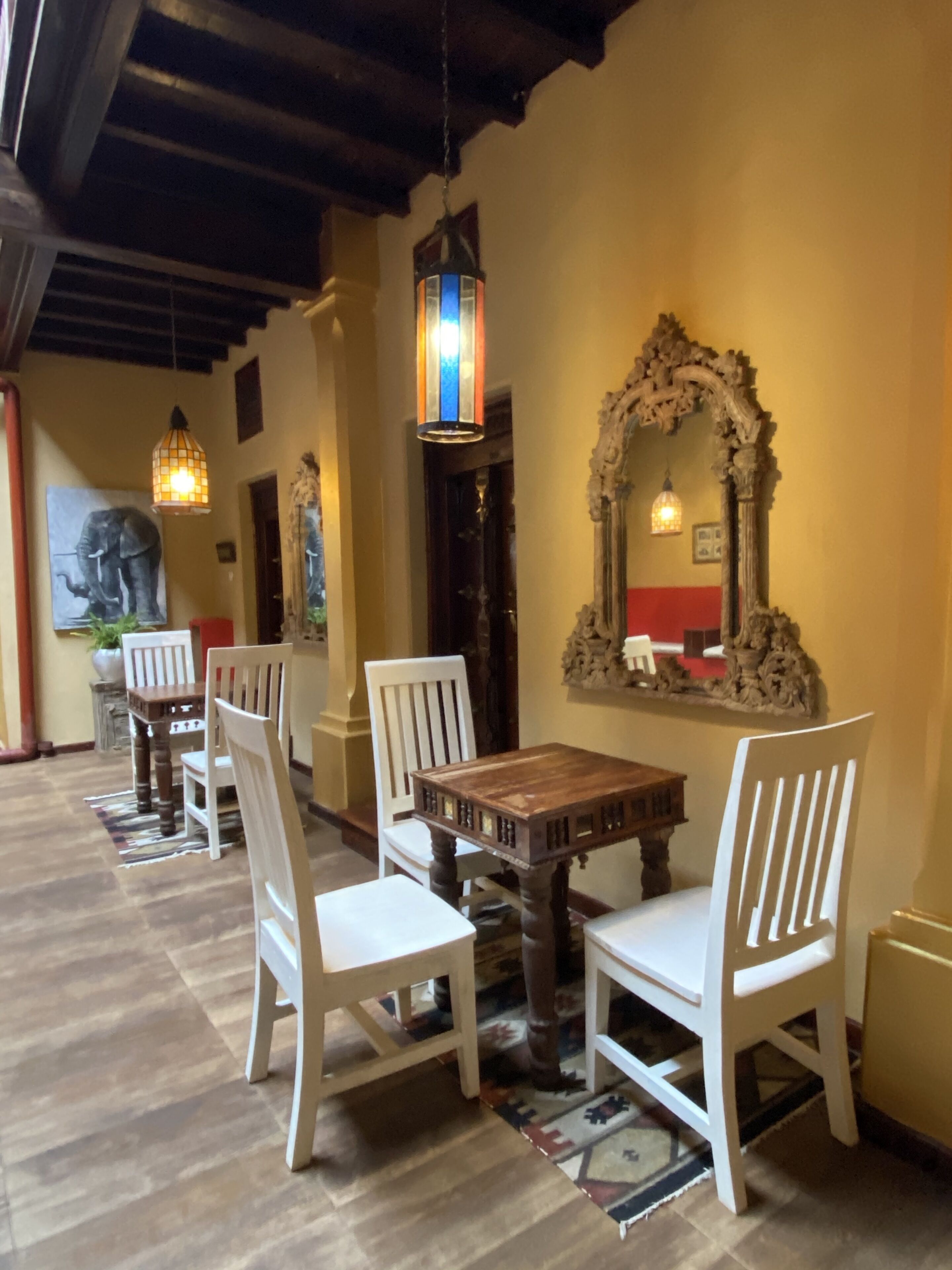 Un coin repas avec une table en bois et des chaises blanches, un grand miroir décoratif et des lanternes suspendues.
