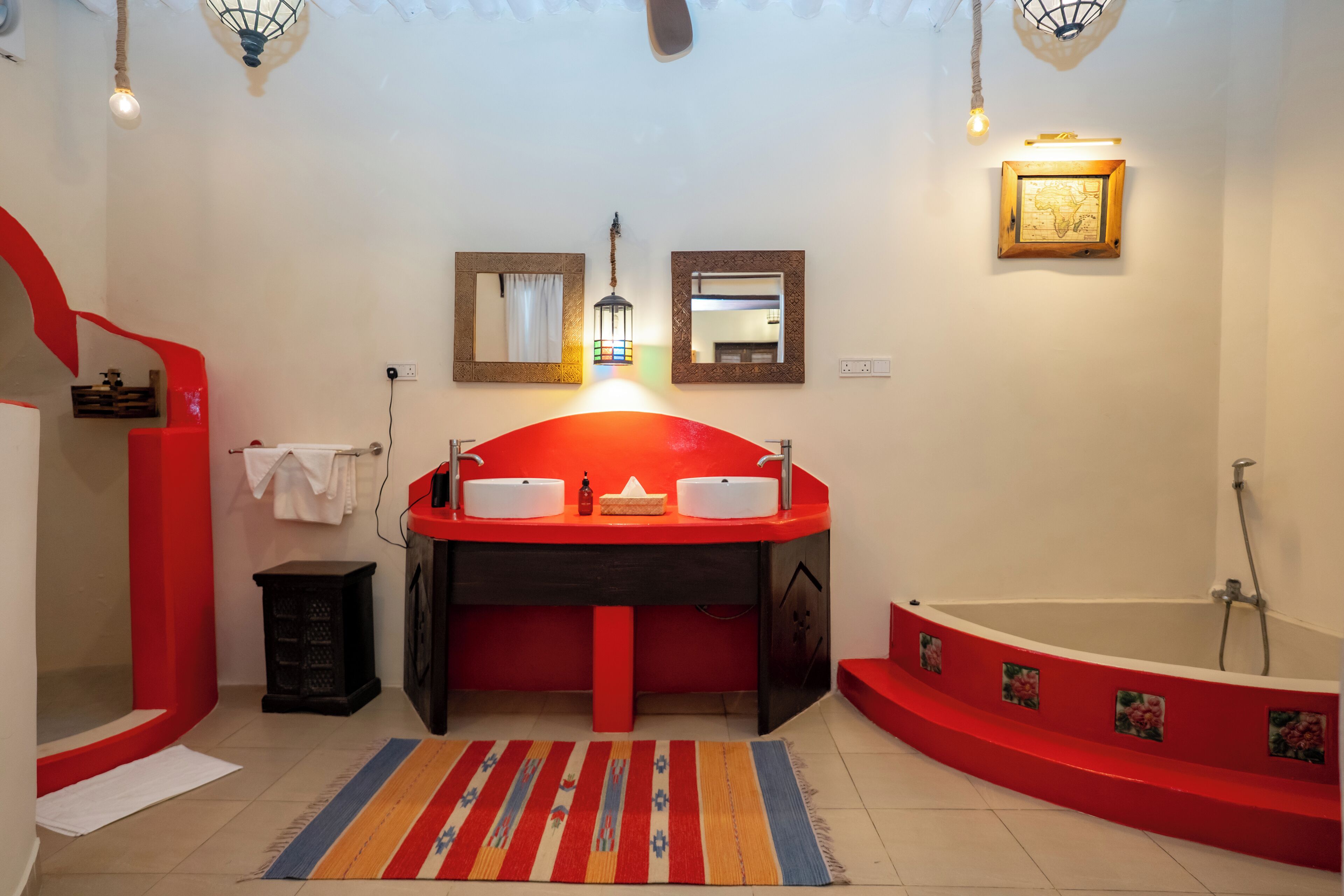 A bathroom with a red sink, two mirrors, a red bathtub, and a colorful rug.