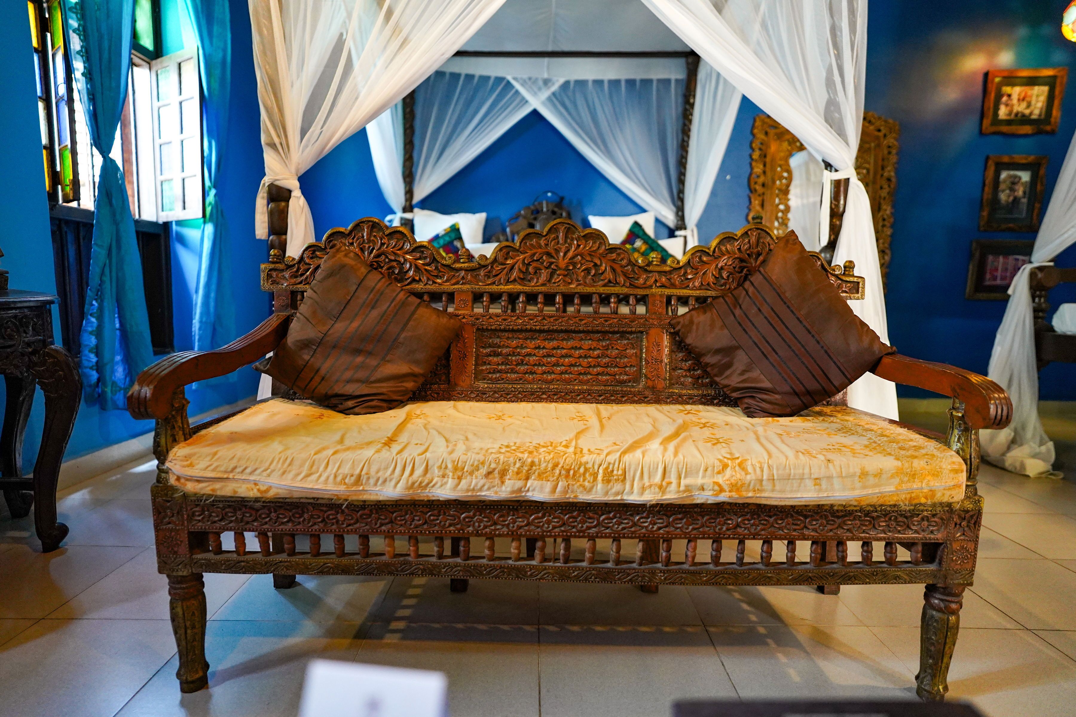 A bed with ornate carvings, a canopy, and a blue wall with framed pictures.