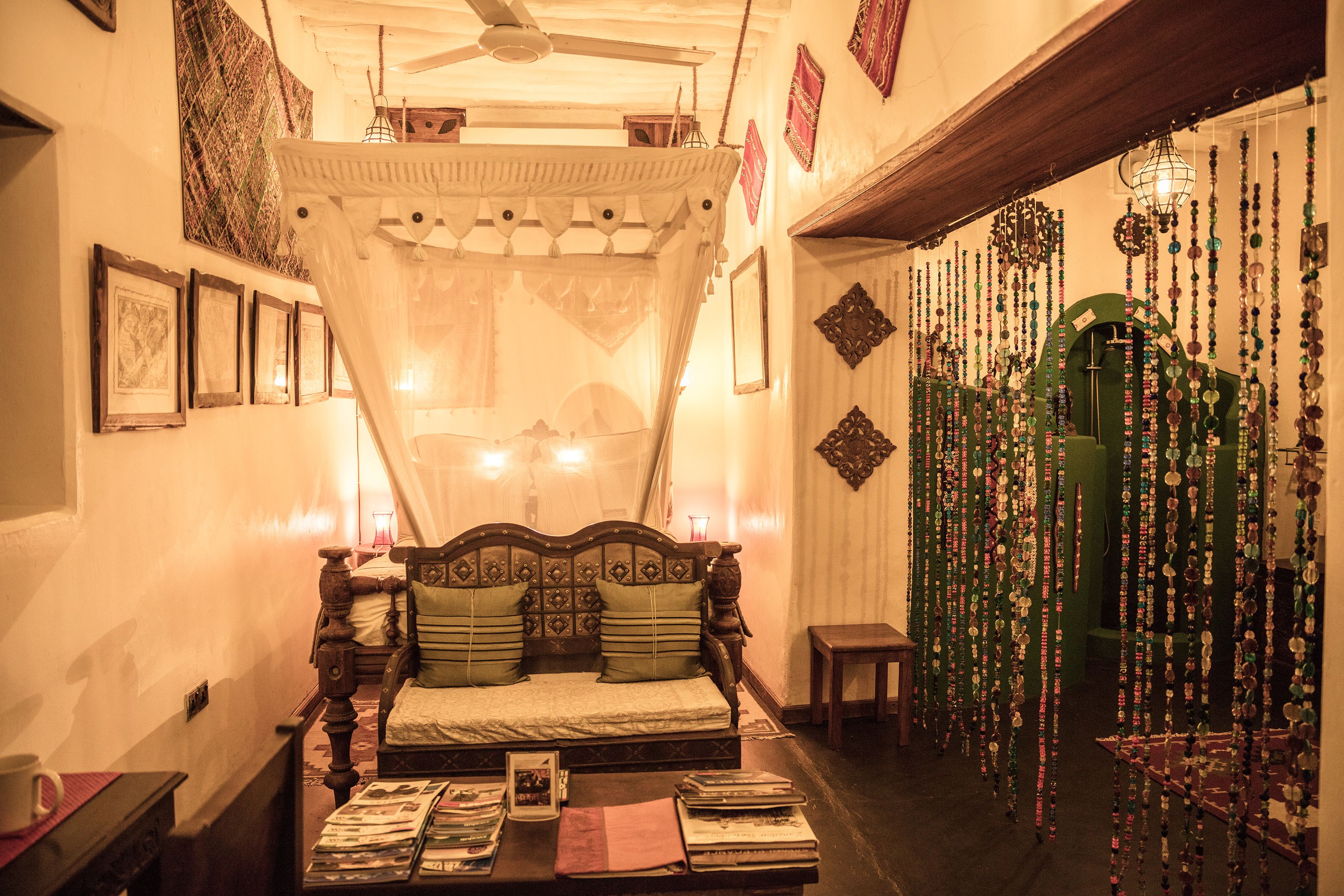 A traditional room with a wooden bed, a small table with books, and a decorative wall with hanging ornaments.