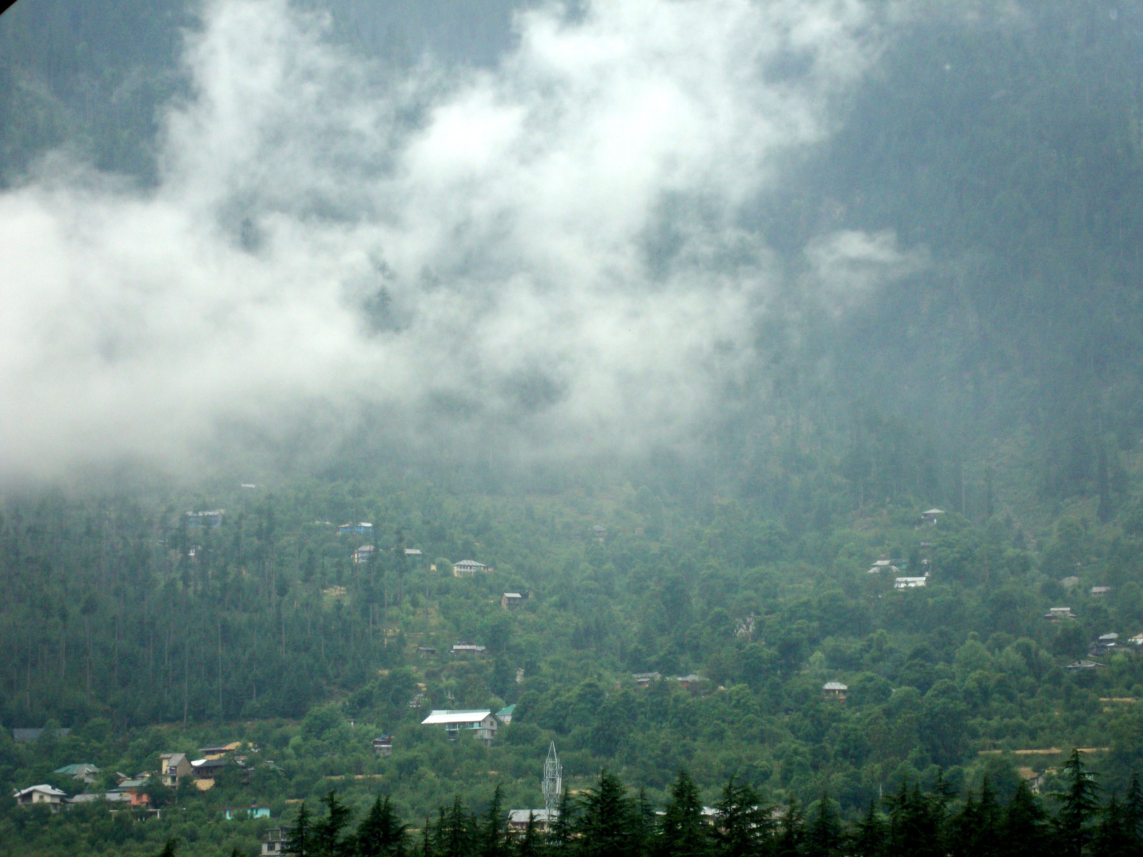A mountainous landscape with scattered houses and dense forest.