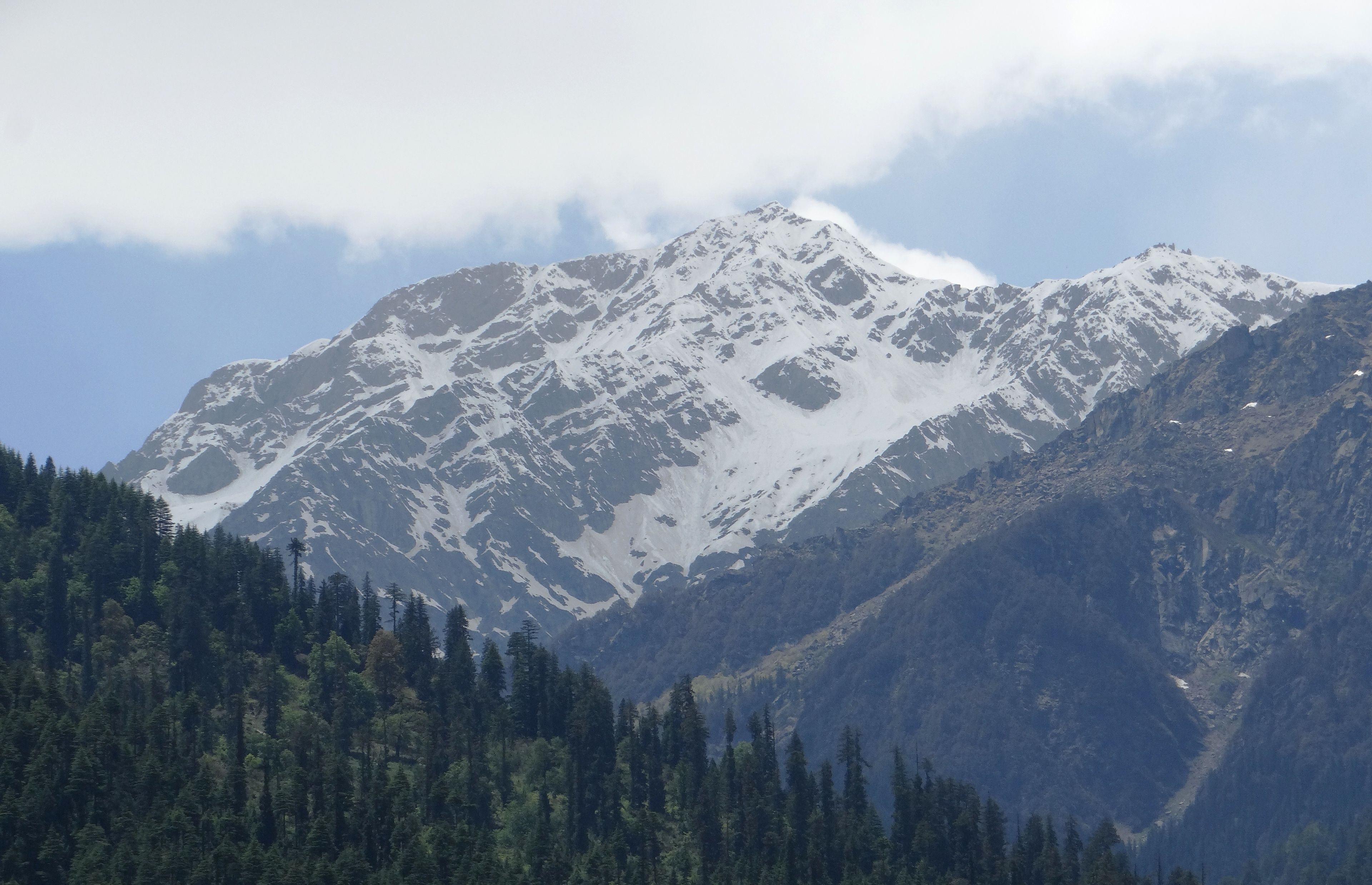 A mountain with snow-covered peaks and a forested foreground.