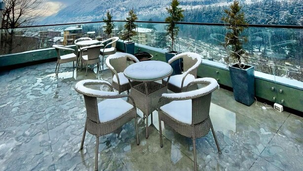 Una terraza con muebles de mimbre y una mesa de vidrio, con vistas a un paisaje nevado y una masa de agua.