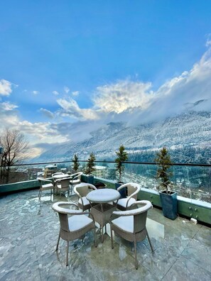 Una terraza con muebles de mimbre y una mesa de vidrio, con vistas a un paisaje nevado y una masa de agua.