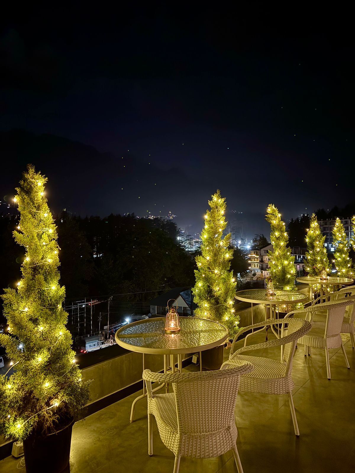 A rooftop terrace with round tables and wicker chairs, decorated with Christmas trees and string lights.