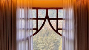 Una habitación con un ventanal grande, con marco de madera y cortinas de tela ligera, que ofrece vistas a un paisaje boscoso.