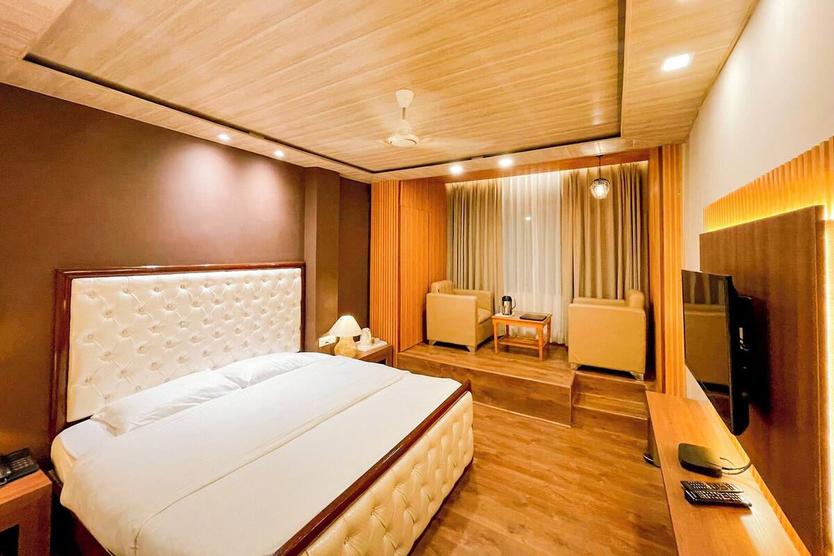 A hotel room with a large bed, a desk, a television, and a seating area with curtains.