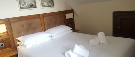 A neatly made bed with white linens and towels, a wooden headboard, and a nightstand with a lamp.