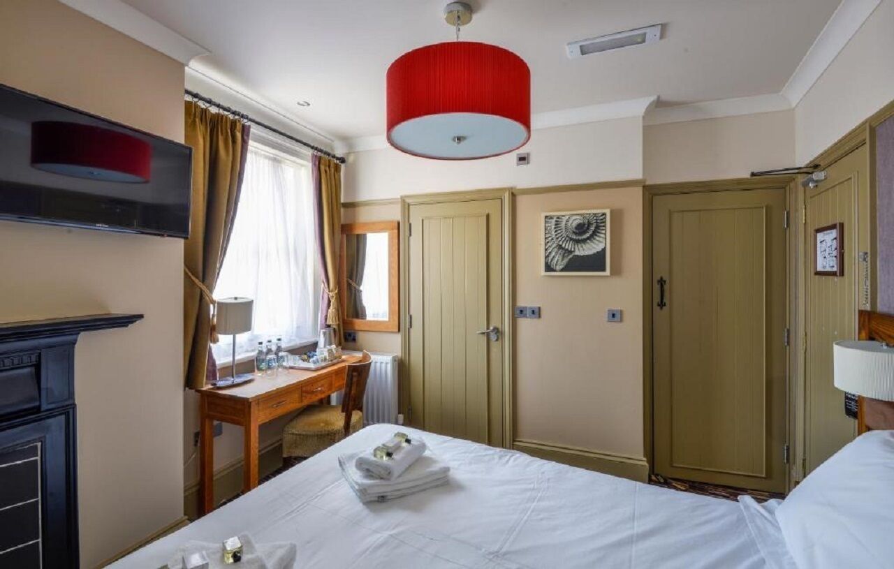 A hotel room with a bed, a desk, a wardrobe, and a red ceiling light.