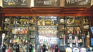 Un bar con estantes llenos de botellas de licores y un cartel que dice 'The Gin Bar' y 'The Winery'.