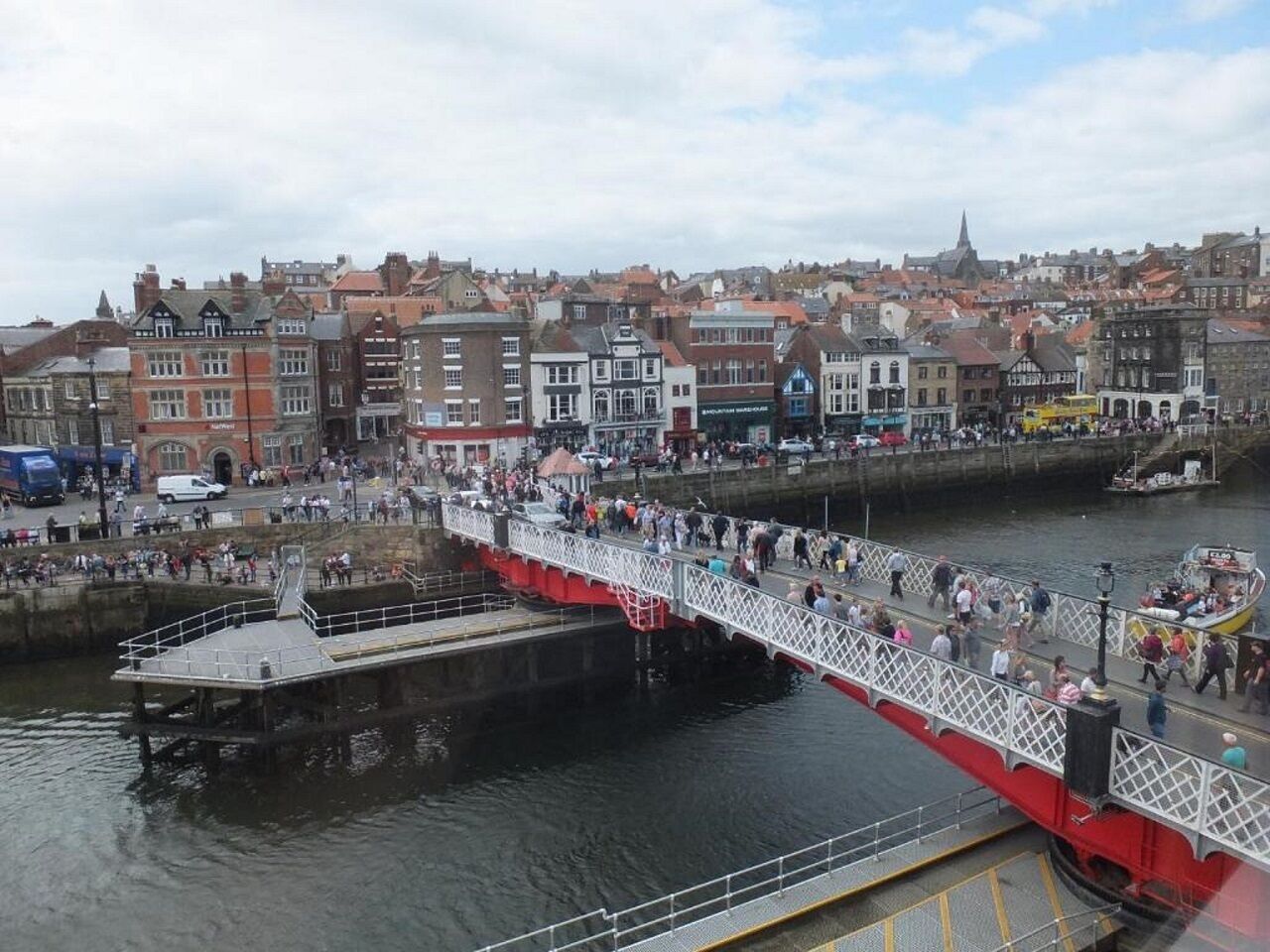 A pedestrian bridge over a body of water with buildings in the background.