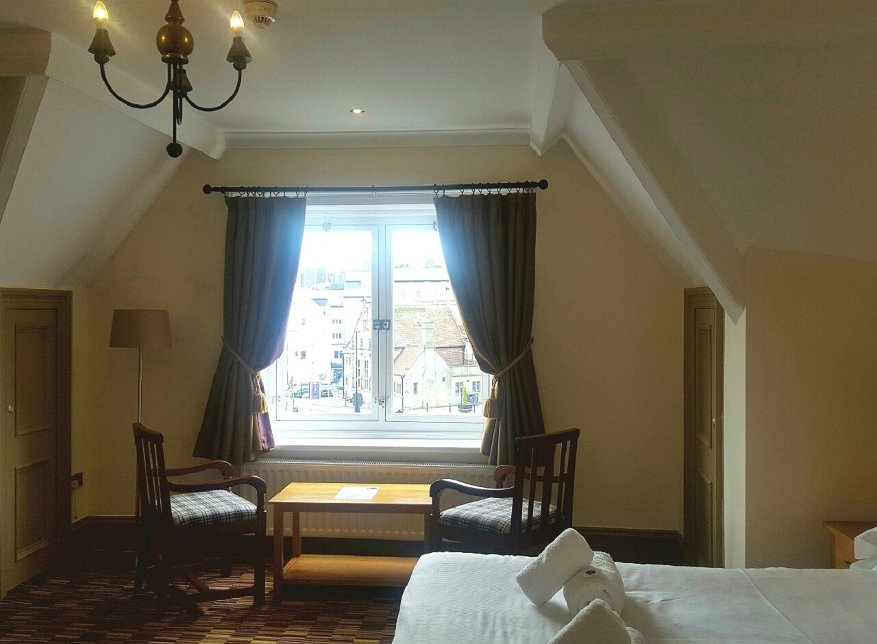 Una habitación de hotel con un ventanal grande, dos sillas, una mesa y una cama.