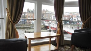 Habitación de hotel con una mesa de madera, dos sillas y vistas a un puente y edificios a través de amplios ventanales.