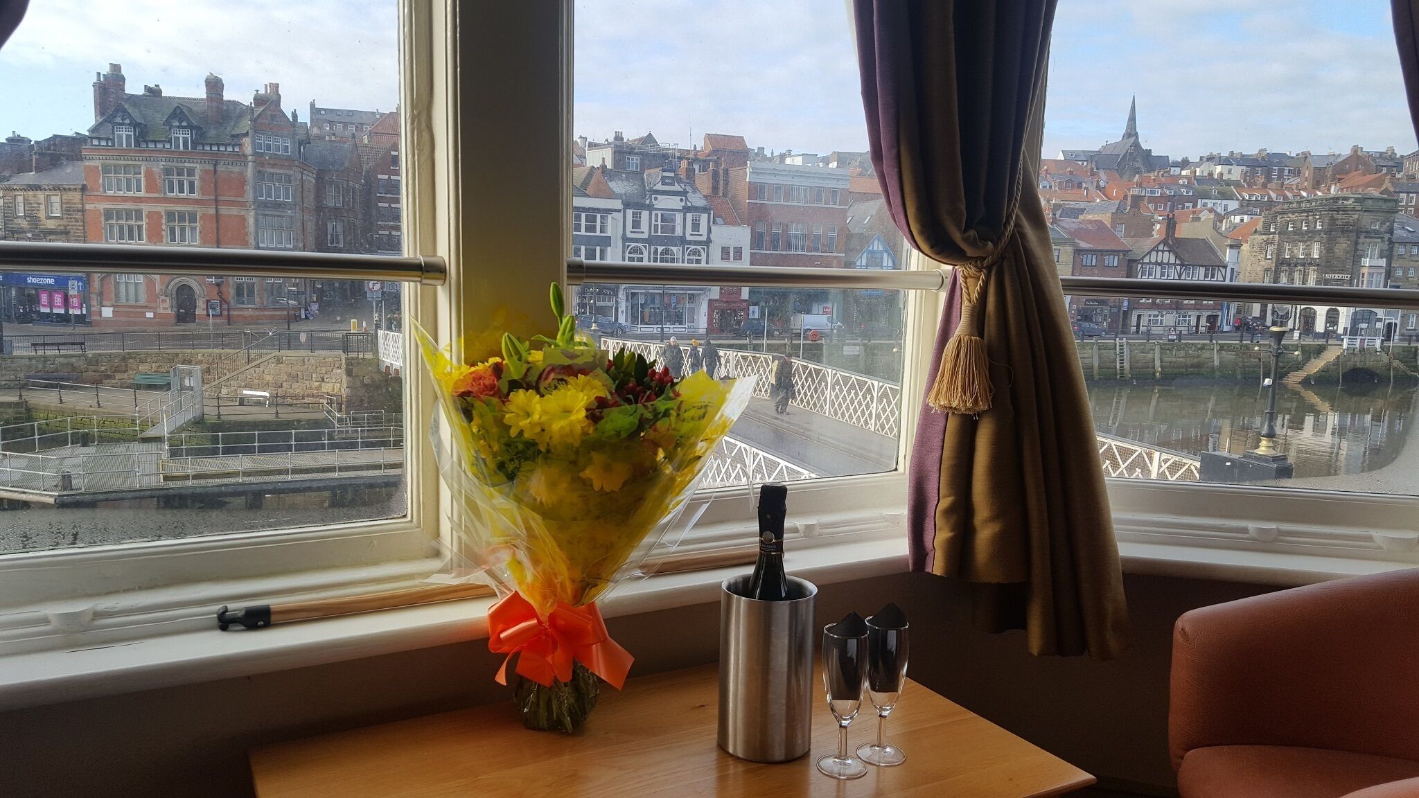 Una stanza con vista sulla città, un bouquet di fiori, una bottiglia e due bicchieri su un tavolo.