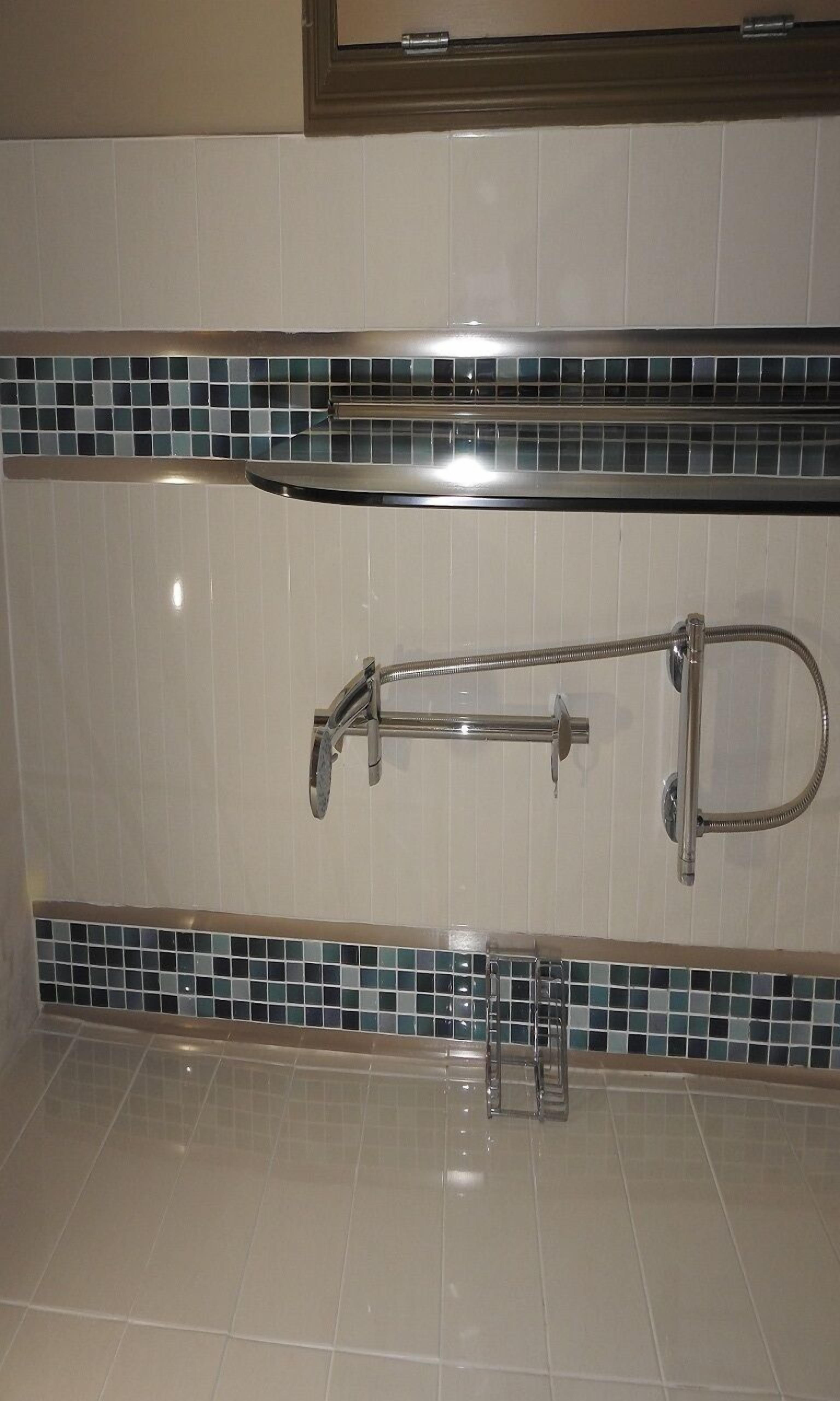 A bathroom with a glass shower enclosure, a handheld showerhead, and a wall-mounted faucet.