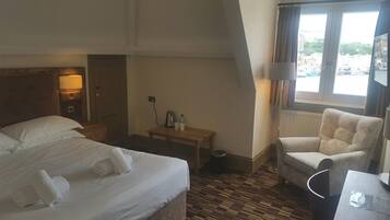 A hotel room with a bed, a chair, a small table, and a window with a view of the city.