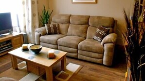 Una sala de estar con un sofá color crema, una mesa de centro de madera y un televisor sobre un mueble de madera.