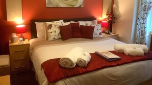 Una habitación de hotel con una cama grande, almohadones rojos y blancos, una manta roja y dos lámparas de noche.