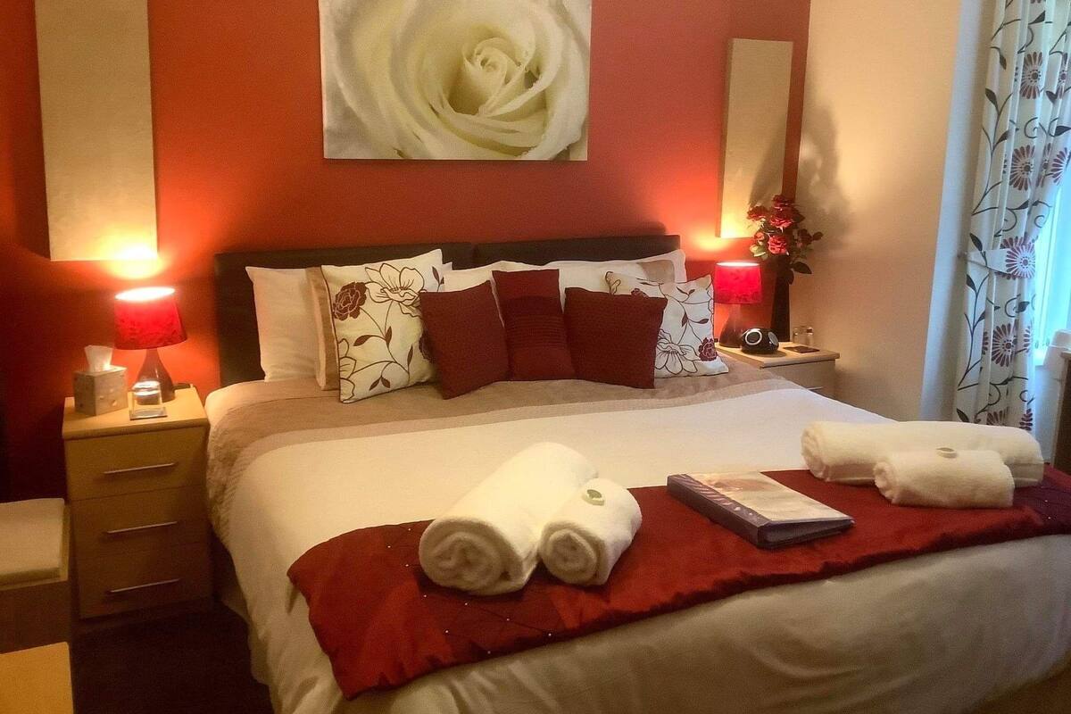 Une chambre d’hôtel avec un grand lit, des oreillers rouges et blancs, un plaid rouge et deux lampes de chevet.