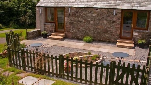 A stone house with a sloped roof, two skylights, and a fenced garden area with outdoor seating. - Ghyll Farm Bed & Breakfast (Frizington)