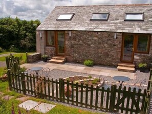 A stone house with a sloped roof, two skylights, and a fenced garden area with outdoor seating. - Ghyll Farm Bed & Breakfast (Frizington)