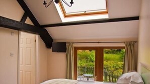 A bedroom with two beds, a skylight, a TV, and a view of a garden. - Ghyll Farm Bed & Breakfast (Frizington)