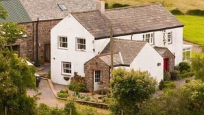 A white two-story house with a stone facade, a red door, and a sloped roof. - Ghyll Farm Bed & Breakfast (Frizington)