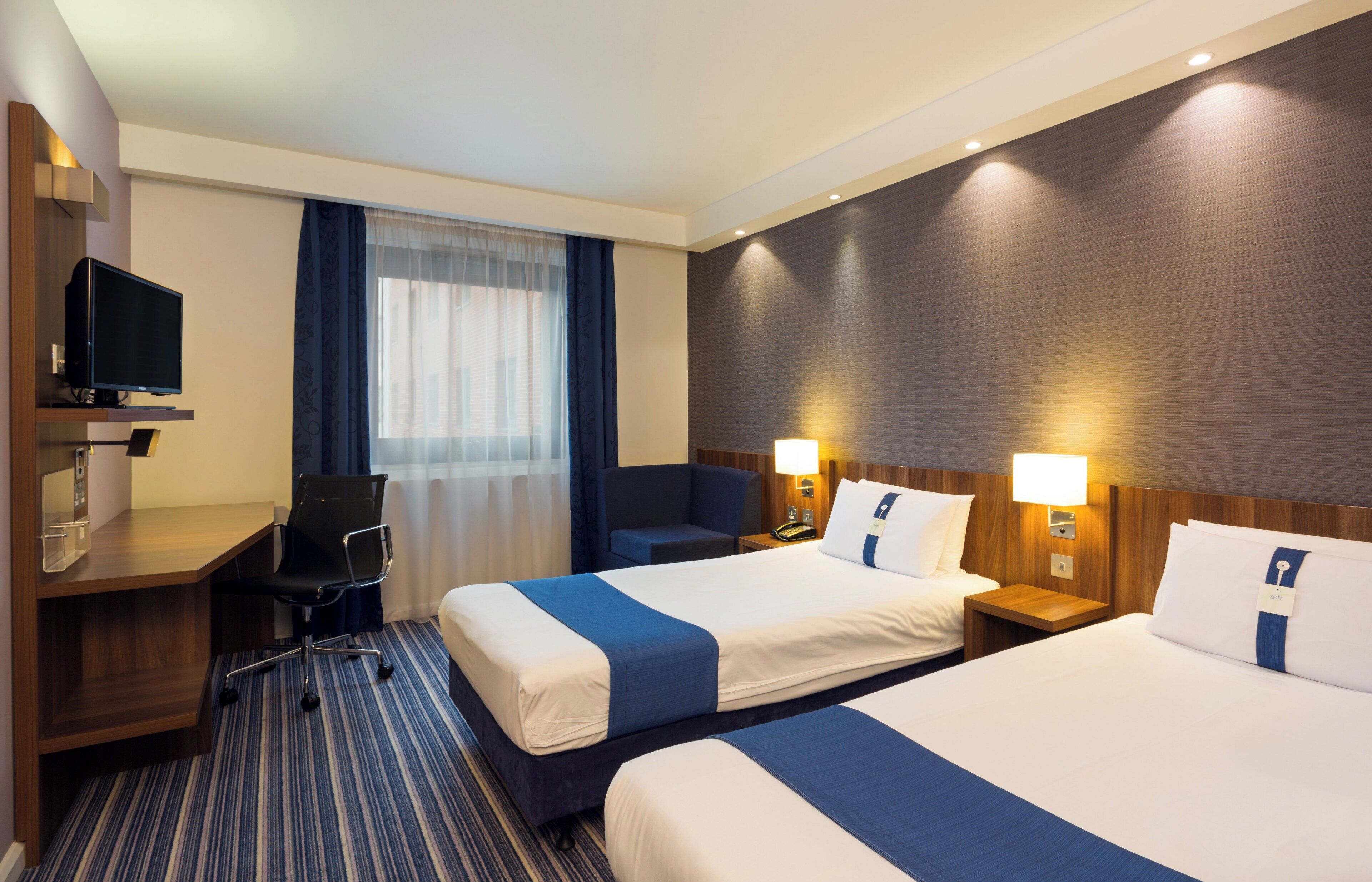 A hotel room with two beds, a desk, a chair, a television, and a window with curtains.