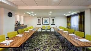A conference room with a long table, yellow chairs, a clock, framed artwork, and a window with curtains. - Holiday Inn Express Harlow by IHG (Harlow)
