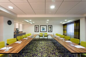 A conference room with a long table, yellow chairs, a clock, framed artwork, and a window with curtains. - Holiday Inn Express Harlow by IHG (Harlow)