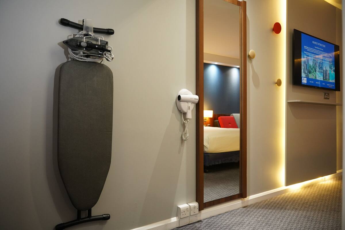 Ett hotellrum med en stor strykbräda, en hårtork och en tv på väggen.