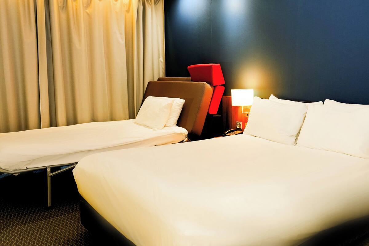 Ett hotellrum med en stor säng, en mindre säng och en röd stol.