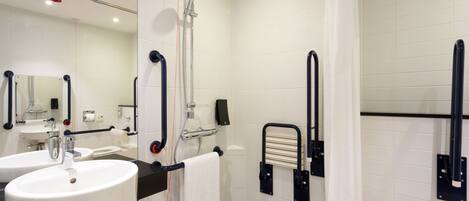 A modern bathroom with two sinks, a shower with a handheld showerhead, and a toilet with a grab bar.