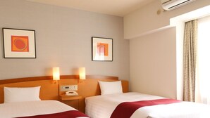 Quarto de hotel com duas camas, uma mesa de cabeceira com telefone e duas luminárias fixadas na parede.