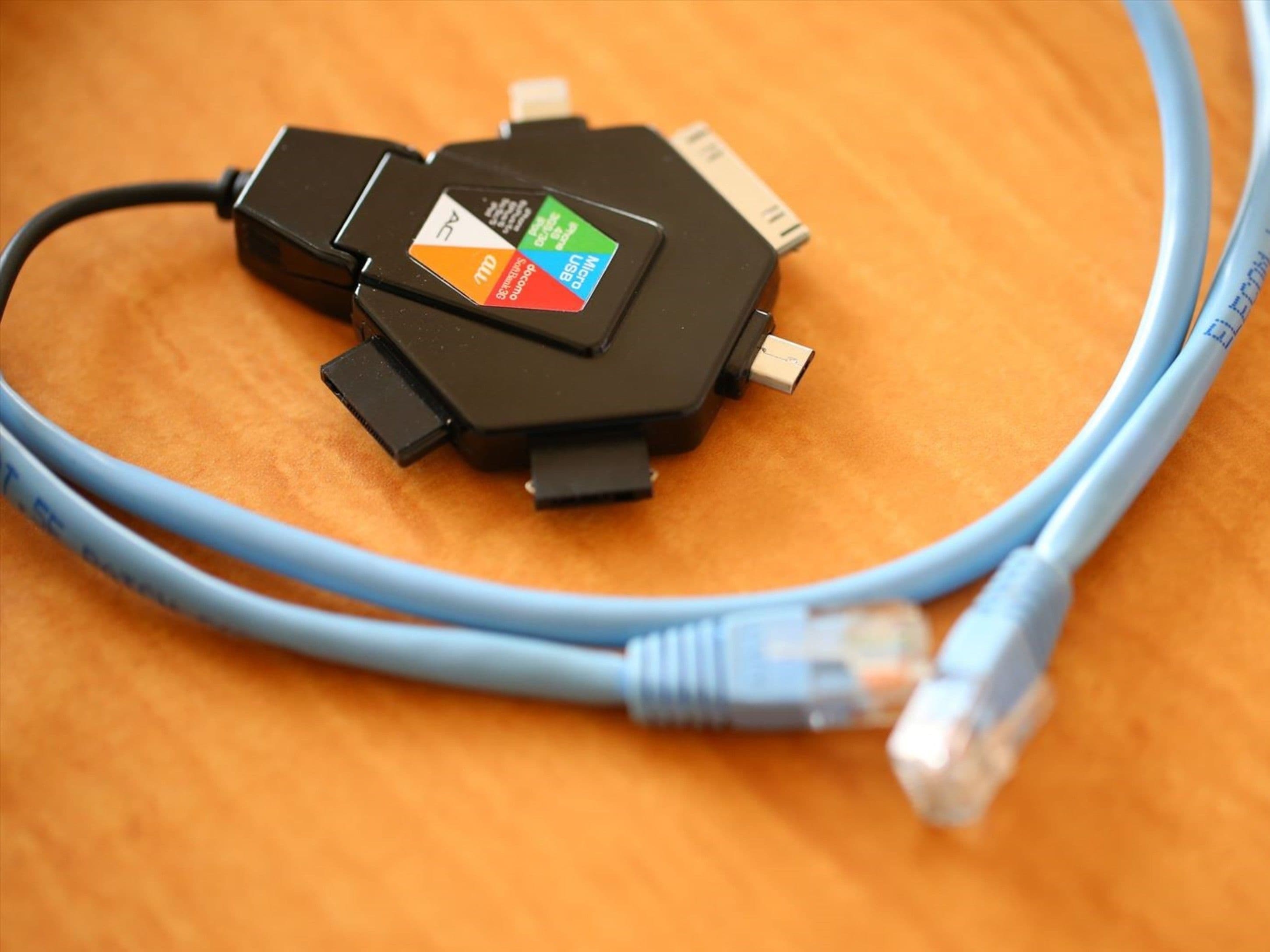 Un dispositivo electrónico negro con un logo y un puerto USB, conectado a un cable Ethernet azul sobre una superficie de madera.
