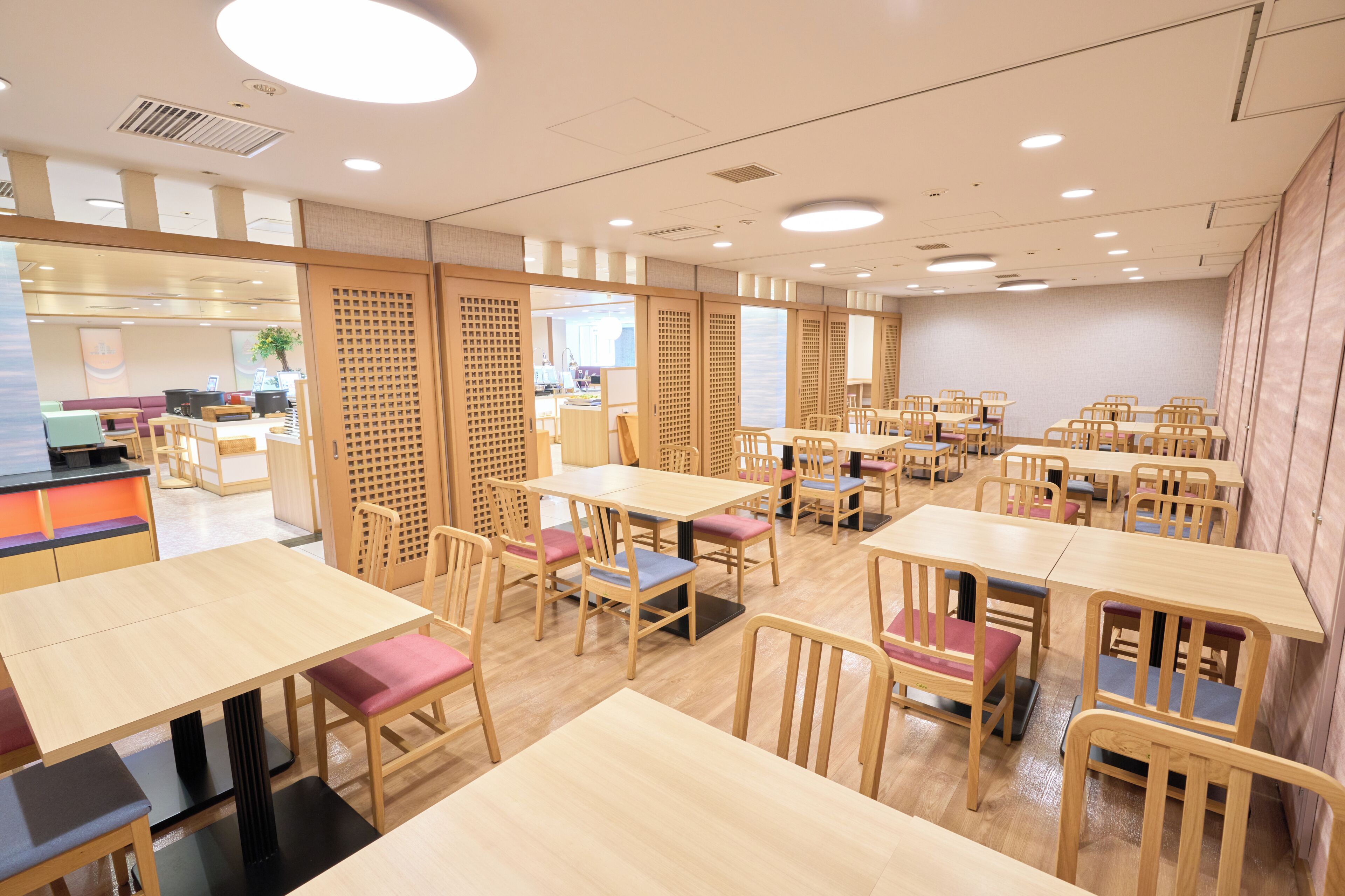 Un vaste espace dédié à la salle à manger, avec de nombreuses tables et chaises, des cloisons en bois et un intérieur lumineux.