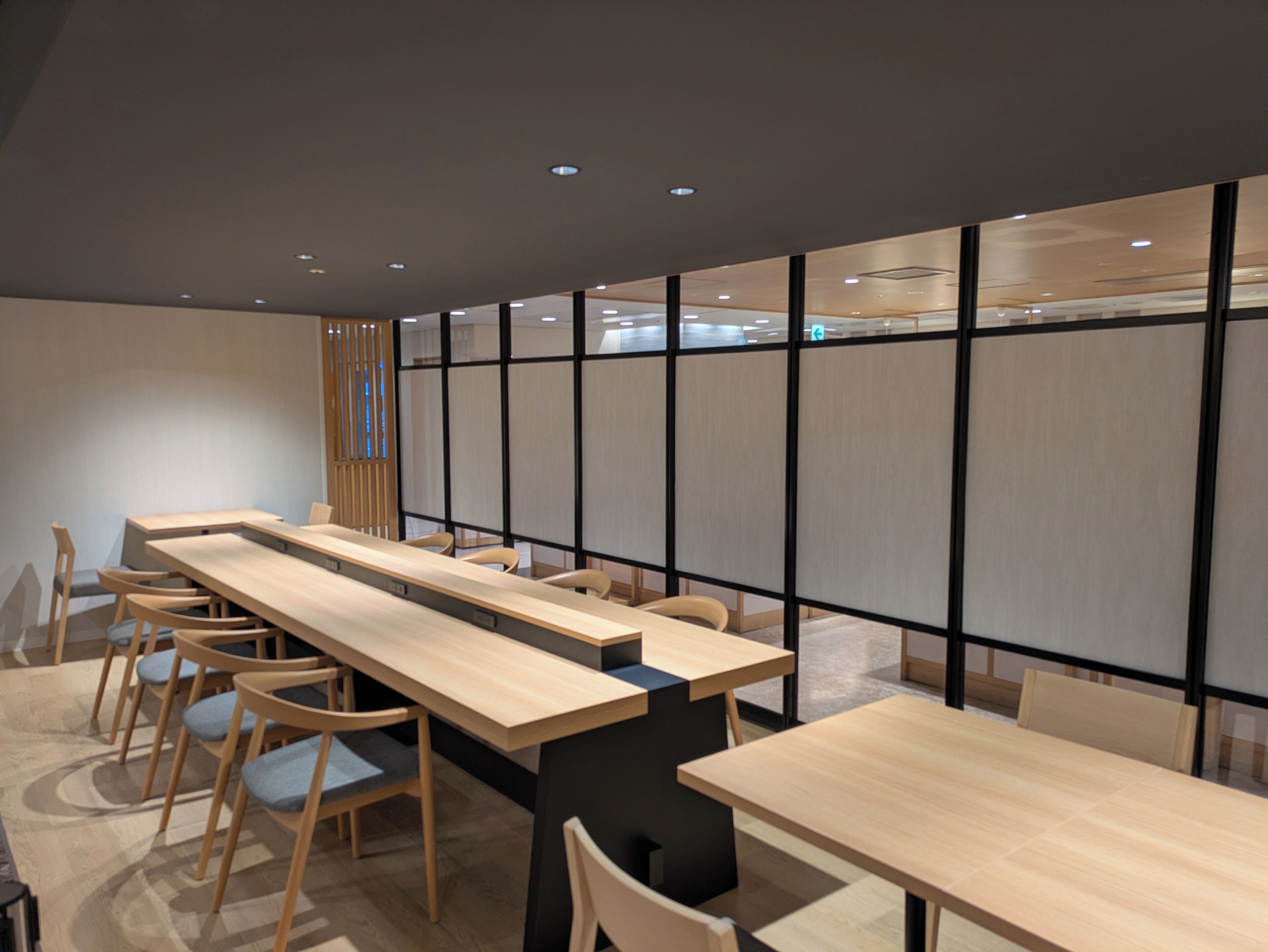 Una sala de conferencias moderna con mesas largas y sillas, separada por una mampara de madera.