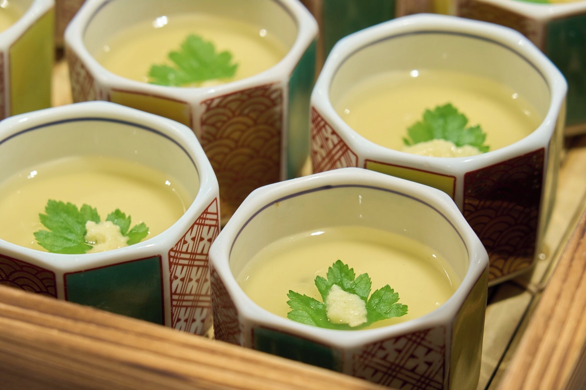 A close-up of several cups of soup with a garnish, arranged on a tray.