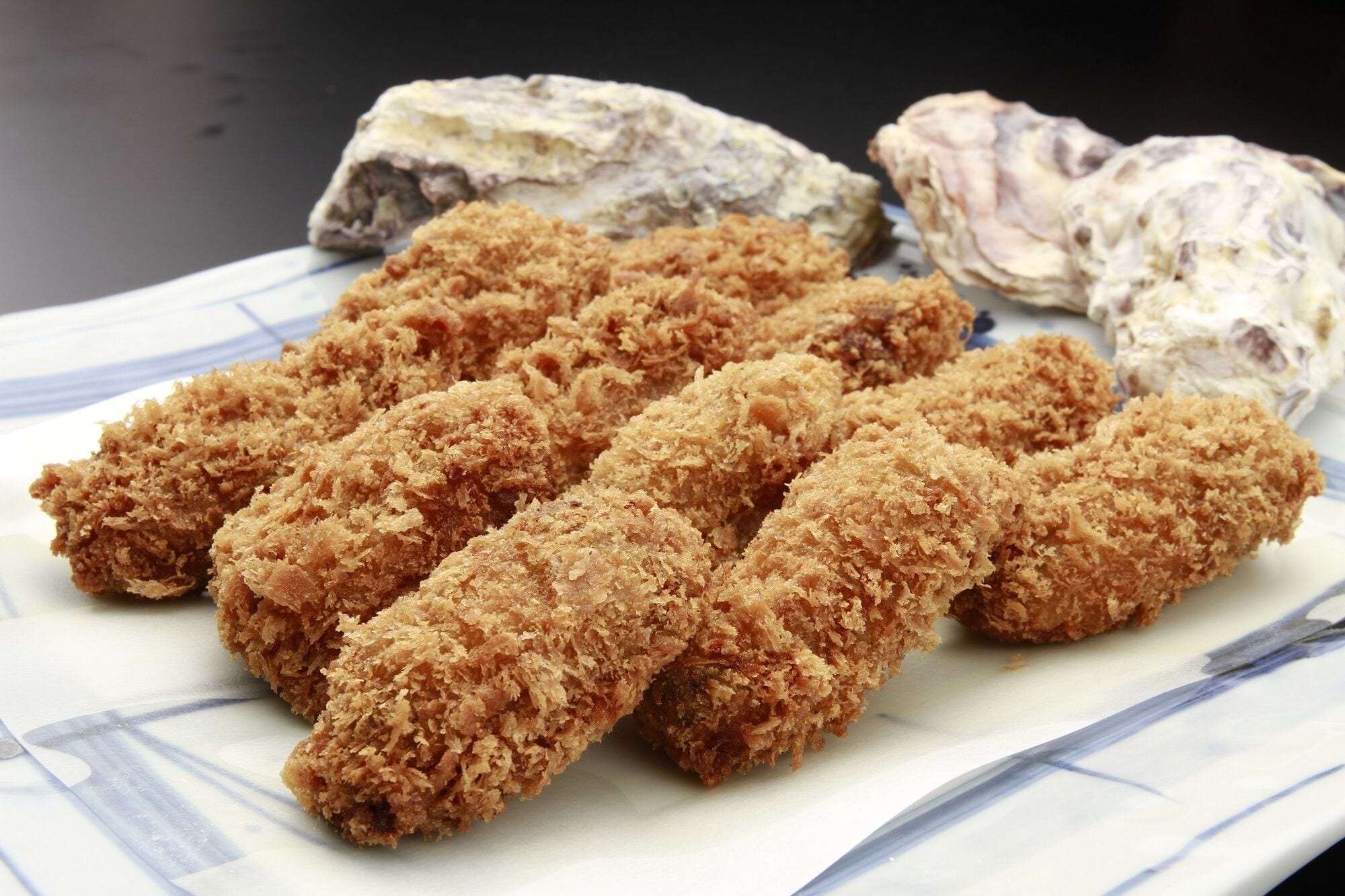 A plate of breaded and fried food items, possibly chicken tenders, accompanied by two pieces of seafood, likely oysters, on a white plate with blue patterns.