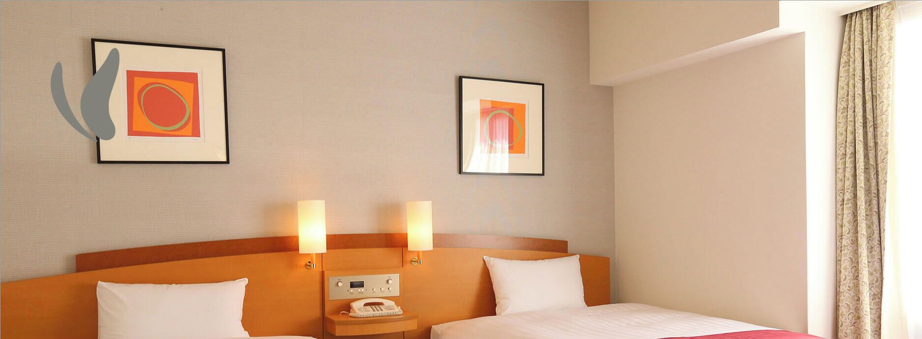 Une chambre d’hôtel avec deux lits, une tête de lit, des lampes de chevet, un téléphone et deux tableaux encadrés au mur.
