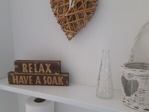 A shelf with a wooden block saying "RELAX HAVE A SOAK," a clear glass vase, and a wicker basket.